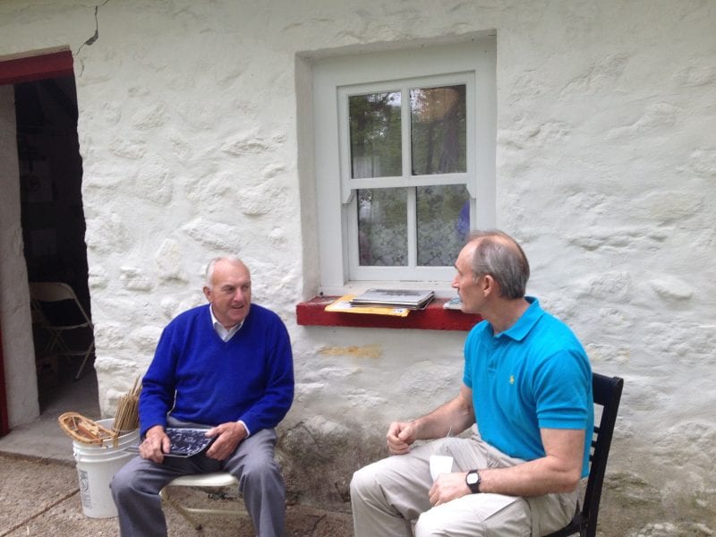 Mike Newell interviewing Johnny Joyce the morning of May 21, 2016, at the Irish Cottage, Irish Cultural Centre 200 New Boston Drive, Canton, MA. Two men seated. Man on left wearing purple sweater over white collared shirt and gray pants, man on right wearing blue polo shirt and khaki pants.