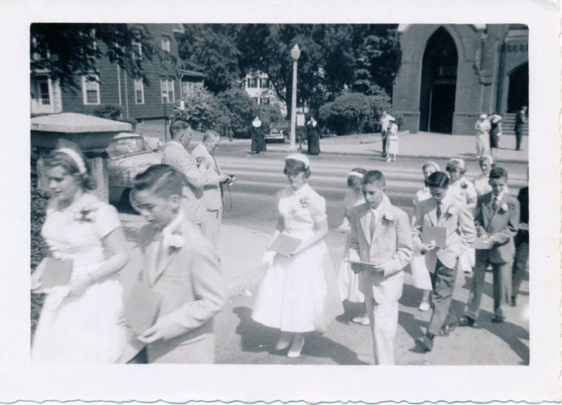 'My eighth grade graduation in 1957 from Saint Mary's School in Winchester--church in background. Pictured: myself Anne Hurley (central figure, girl in white gress, lamp post sticking out of her head).'