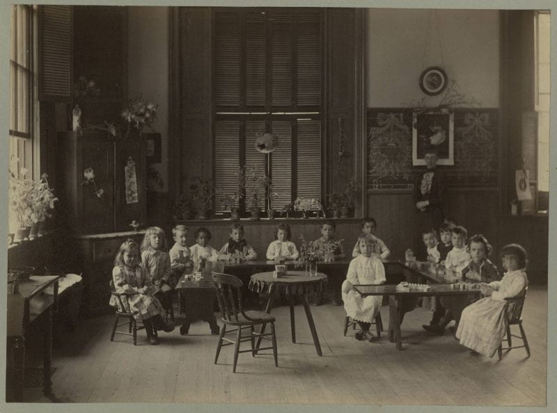 Black-and-white photo of children sitting at tables in a classroom