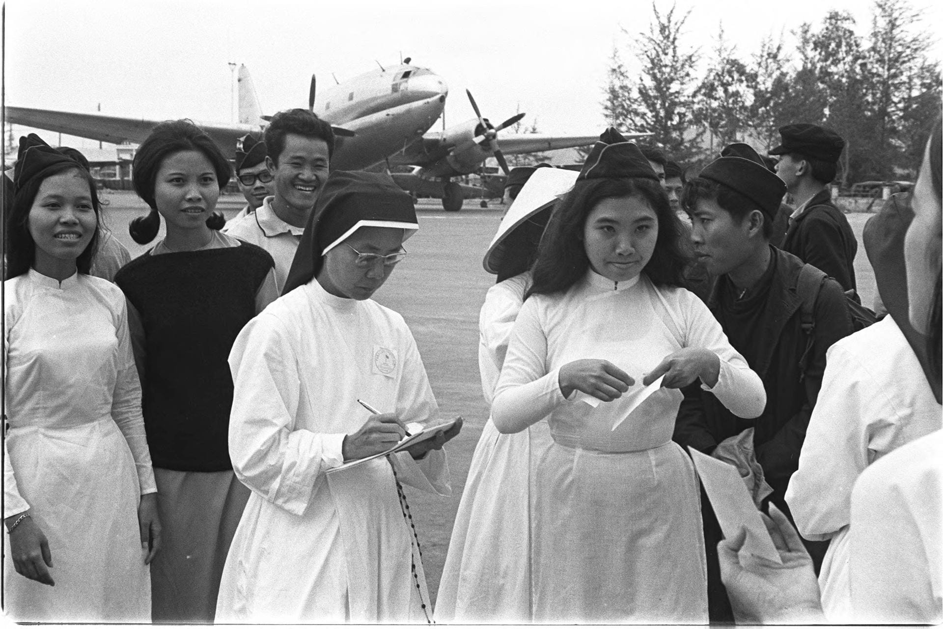 Black-and-white photo of several people standing outside with an airplane in the background