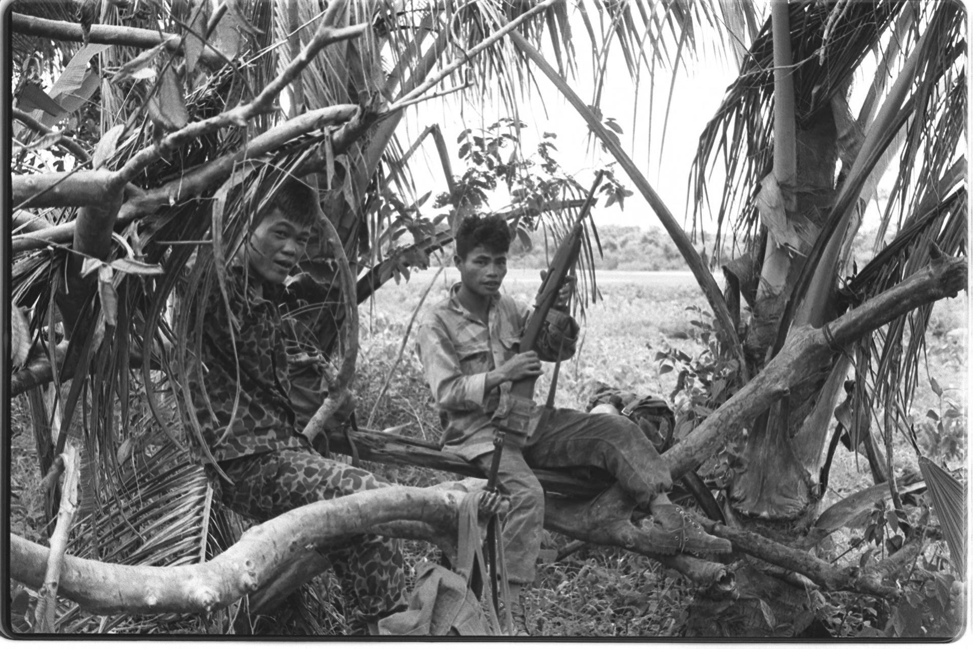 Black-and-white photo of two soldiers sitting between trees