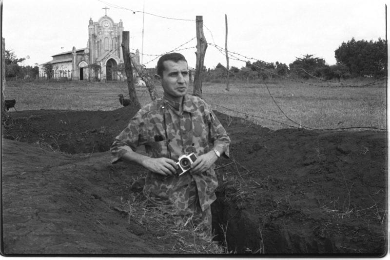 Black-and-white photo of Francois Sully standing in a foxhole holding his camera
