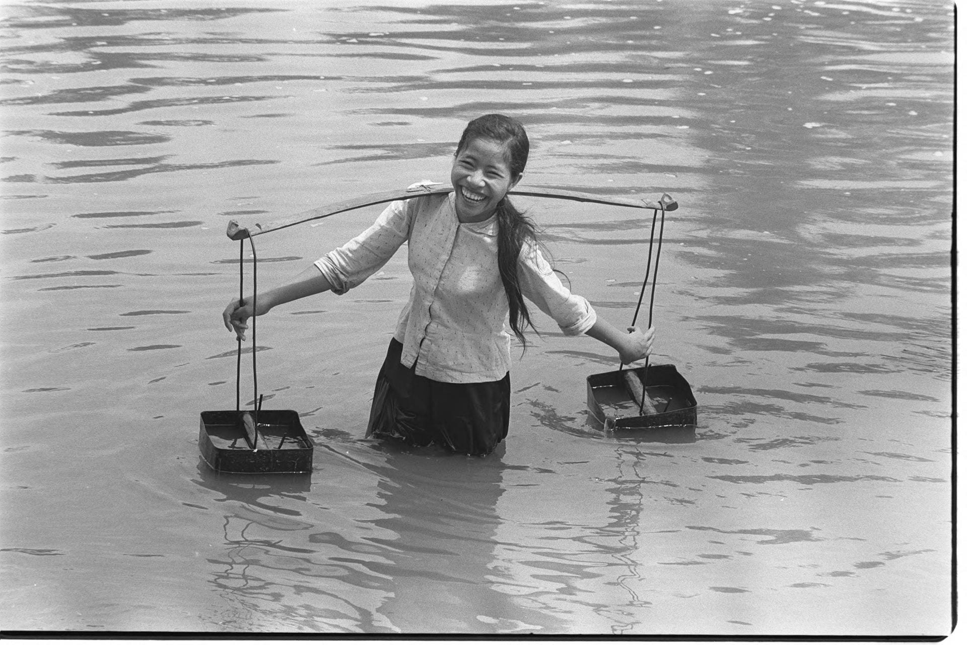 Black-and-white photo of a girl standing in a river with two pails of water