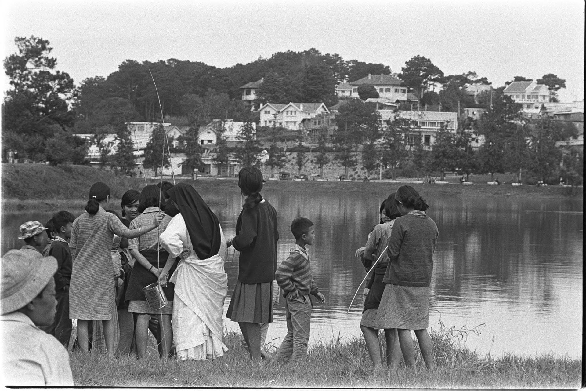Black-and-white photo of several people standing on the bank of a river with fishing poles