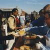 Color photograph of people being served food at an outdoor buffet line