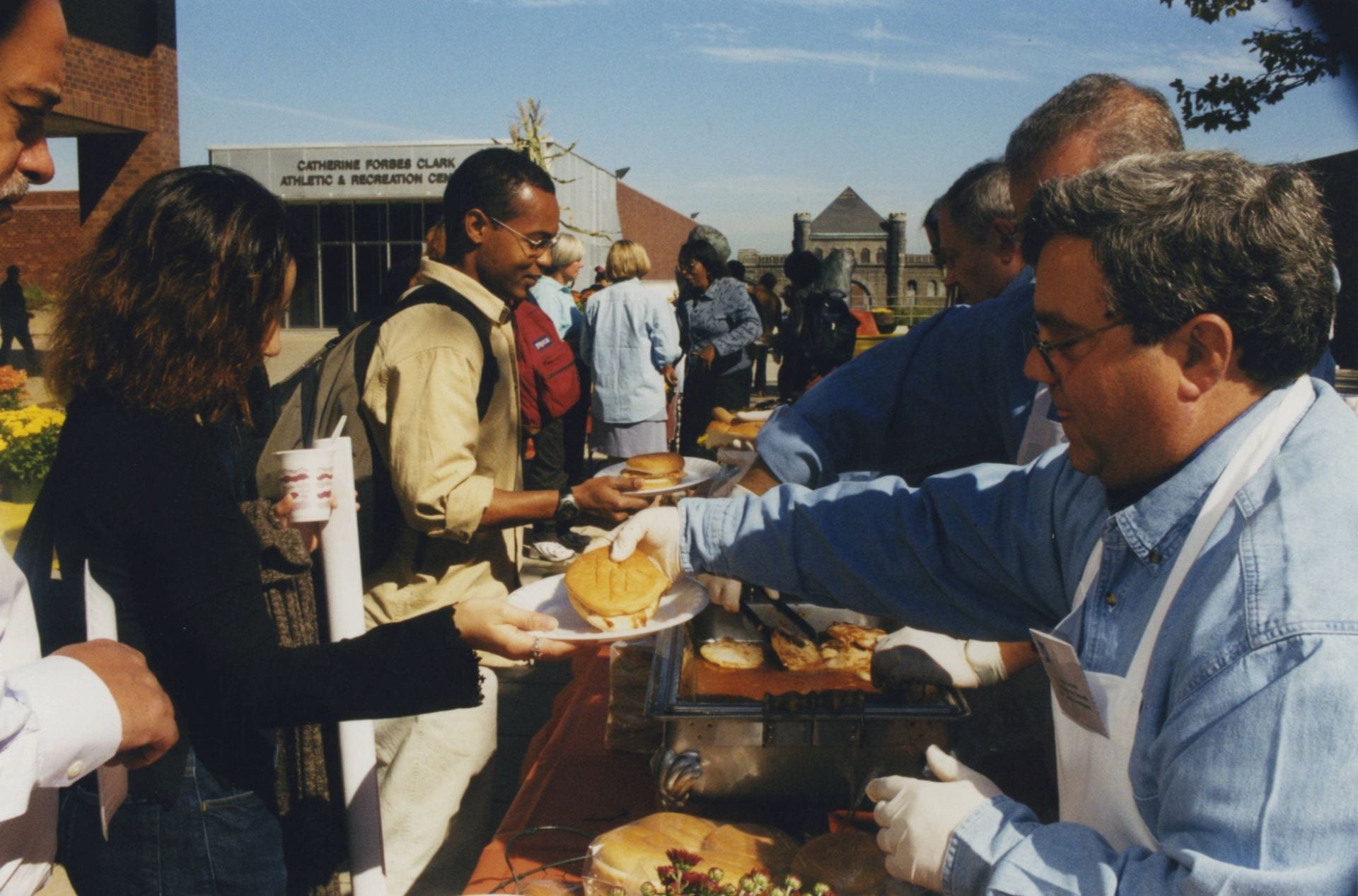 Color photograph of people being served food at an outdoor buffet line