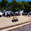 Color photograph of people looking at poster displays on the UMass Boston campus, with a few people sitting on steps in the foreground