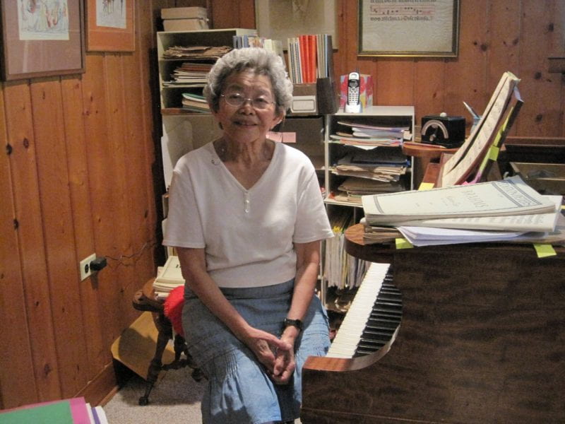 Alice Setsuko Inamoto Takemoto sitting at a piano, smiling with her hands folded in her lap
