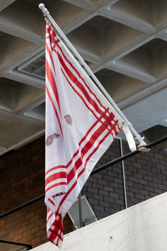 Side view of a red and white flag hanging from a railing.