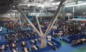 An overhead view of the convention center with many tables, chairs and people inside at the conference