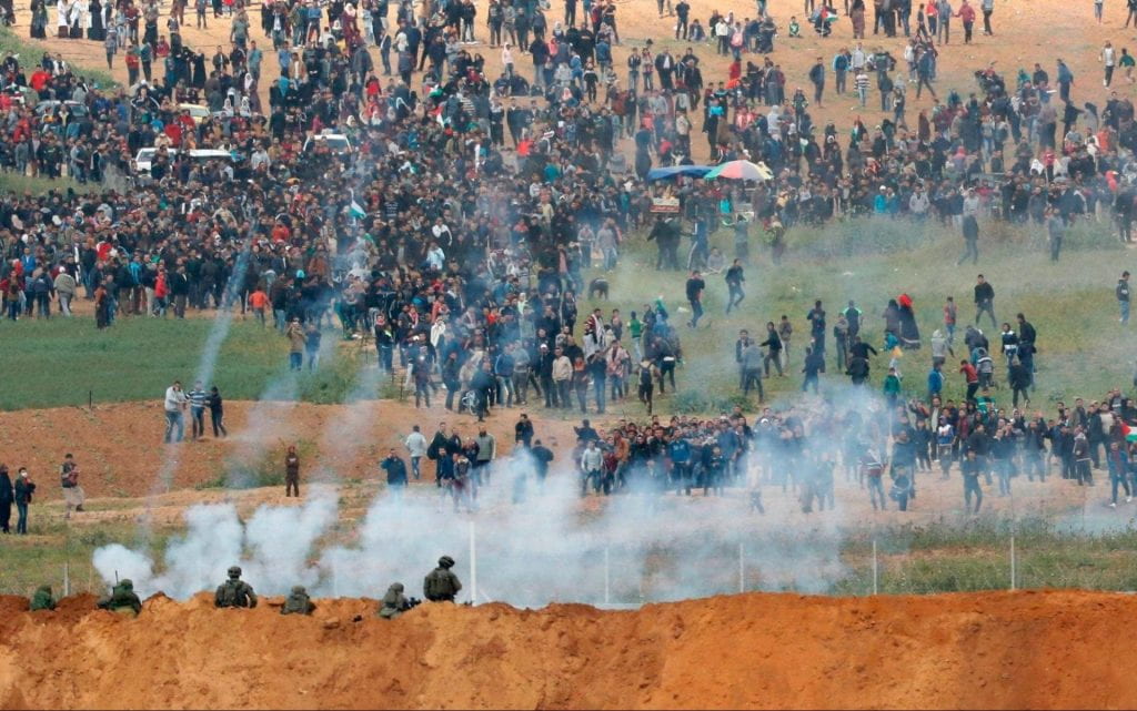A photograph of a large group of protesters facing tear gas from a police force in an unknown location