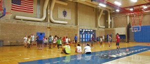 Handful of students mentors sit, jump rope and talk on the floor while a pool of students stand and dance in the gym to celebrate their last day of camp.