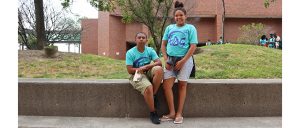 Two students (male and female) pose in front of stairs with their blue TAG t-shirts!