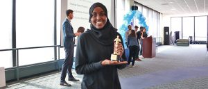 Student with hijab poses with trophy in her hand as she makes way to her seat. 