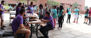 Students line up for lunch by picnic table where mentors in purple t-shirts sit.