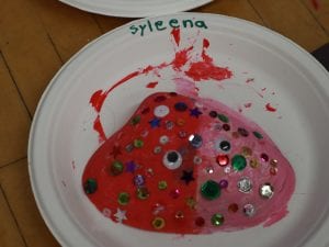 A sea shell that is decorated with different colors of pebbles and painted pink and red.