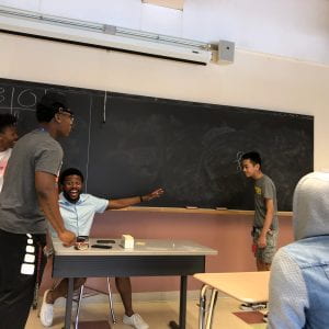 Student drawing on board without facing it, surrounding students in shock of his ability.