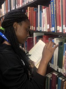 Student reading book by library shelves.